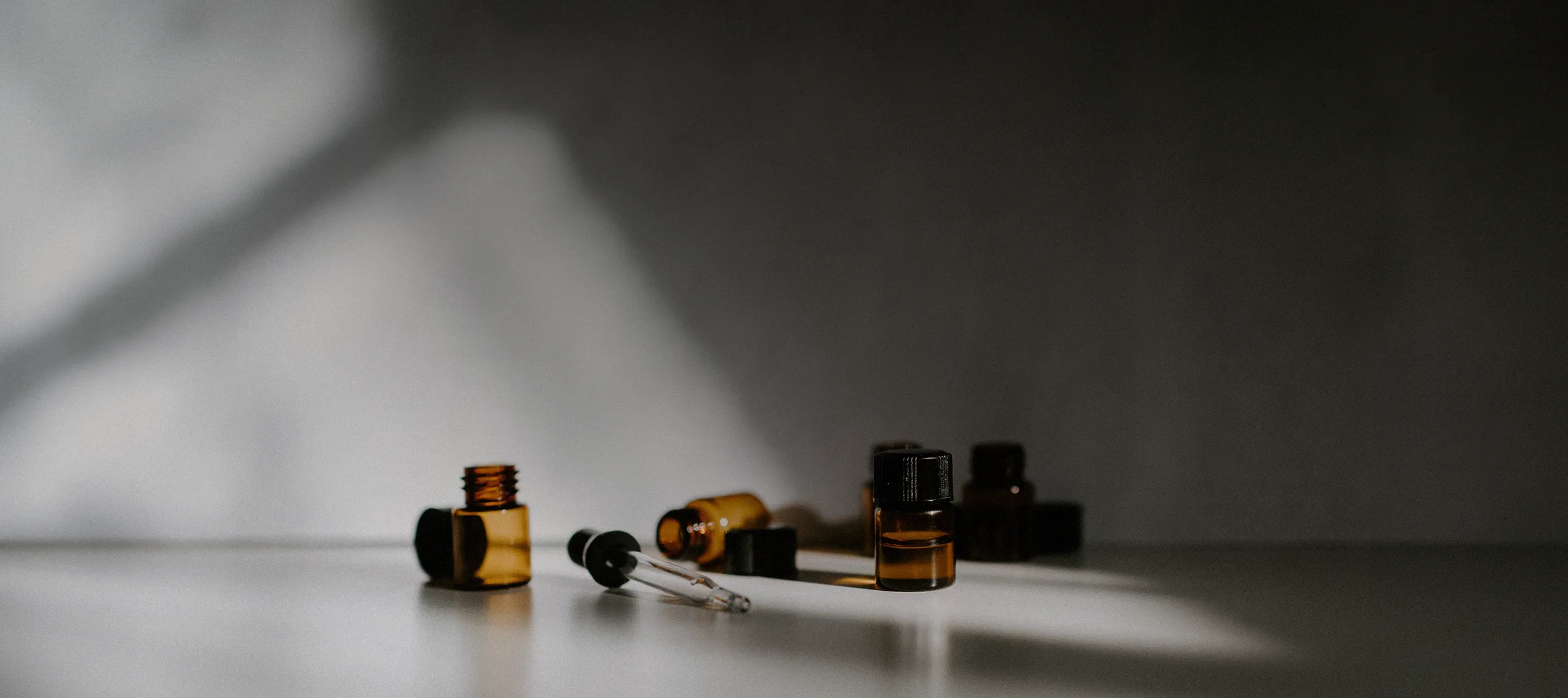 Small amber fragrance bottles on grey background with natural light casting across the scene